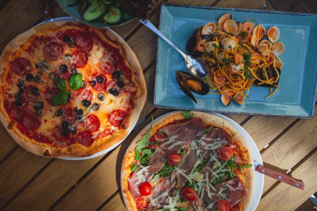 Top view of delicious pizzas and seafood pasta, perfect for Italian food enthusiasts. Captured in natural light.